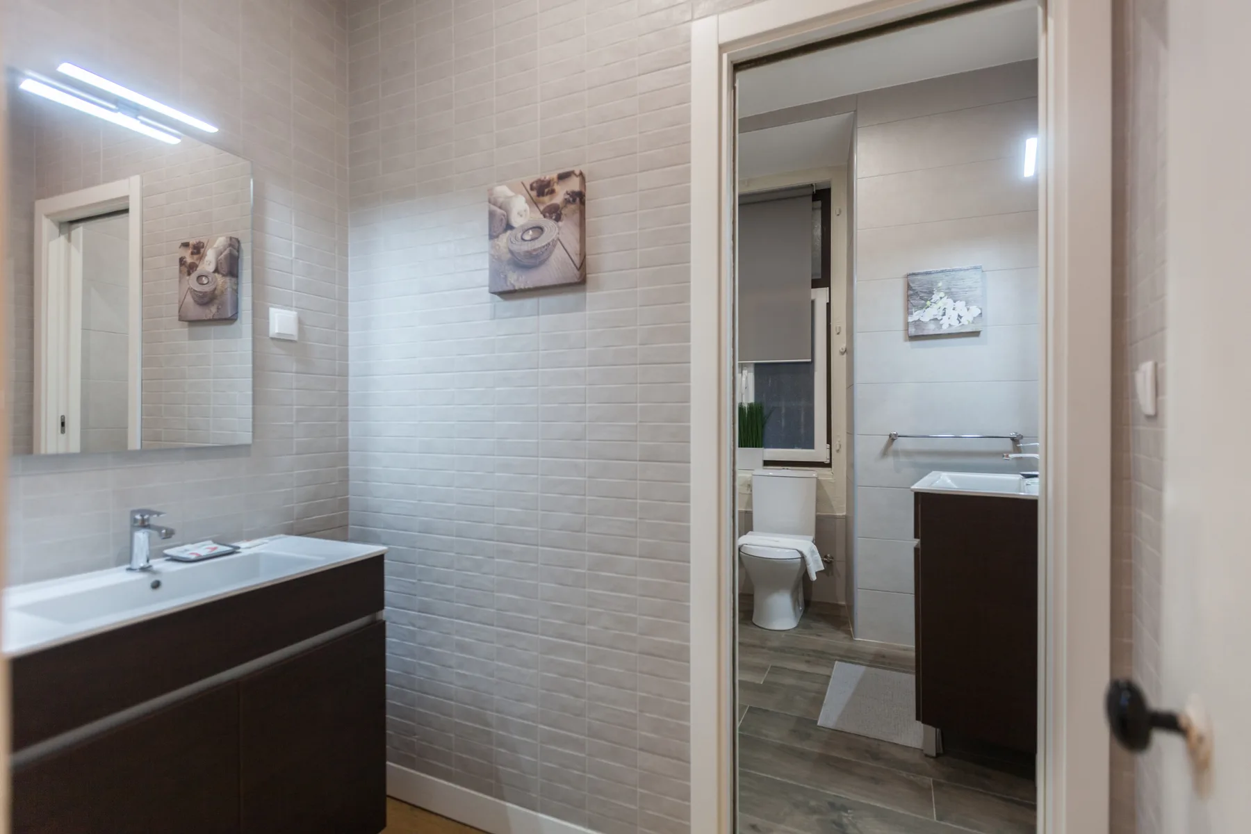 A tiled bathroom with a sink and a doorway opening onto another bathroom area.