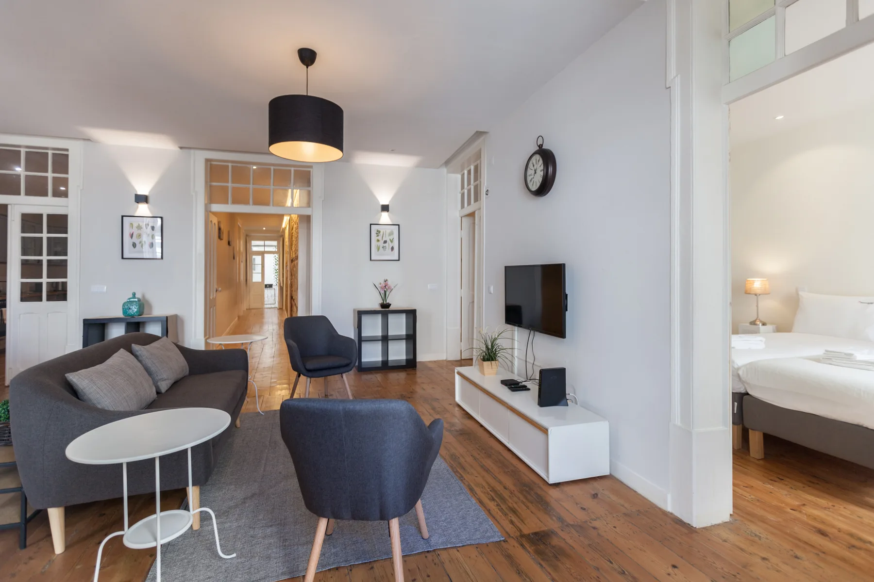 A bright living room with seating, a television, and a bedroom visible through the doorway.
