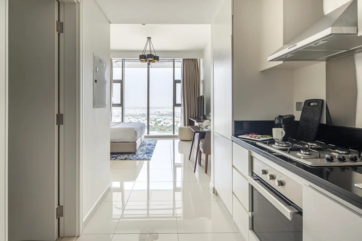 Un interior luminoso muestra una cocina compacta junto a un dormitorio con grandes ventanas.