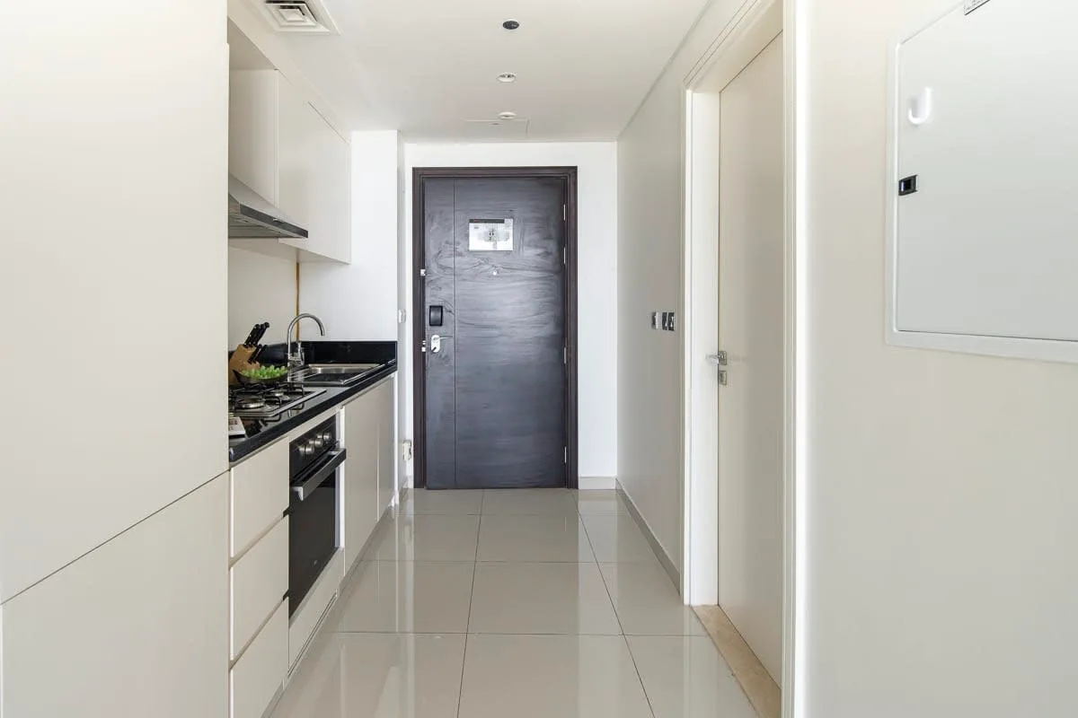 Una cocina estrecha y un pasillo conducen a una puerta de entrada oscura.
