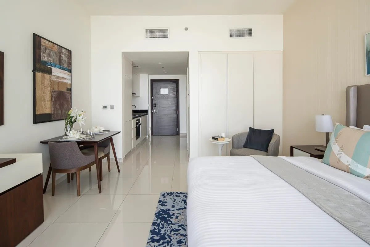 A bright bedroom with a neatly made bed and a small dining area.