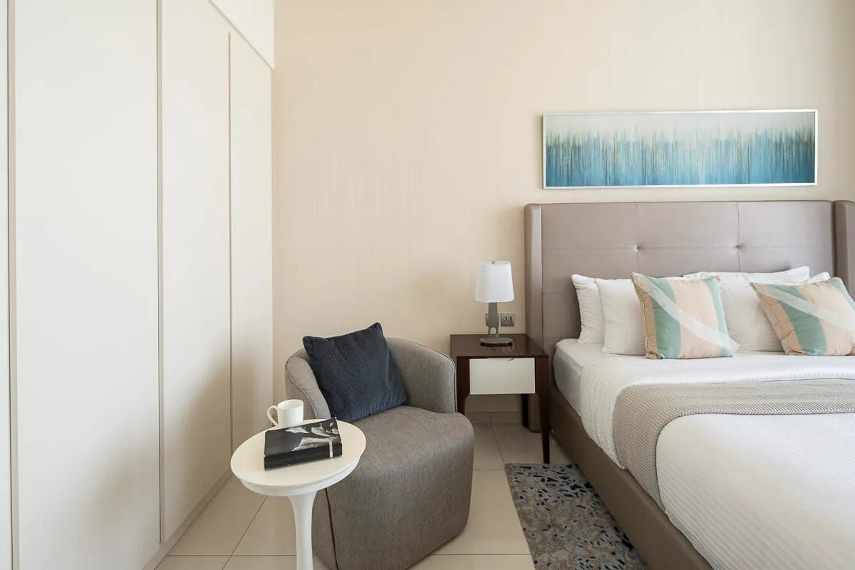 Un dormitorio luminoso con una cama, asientos tapizados y una pequeña mesa auxiliar.