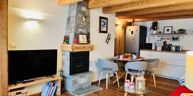 A combined living and dining area with a television, fireplace, and kitchen in view.