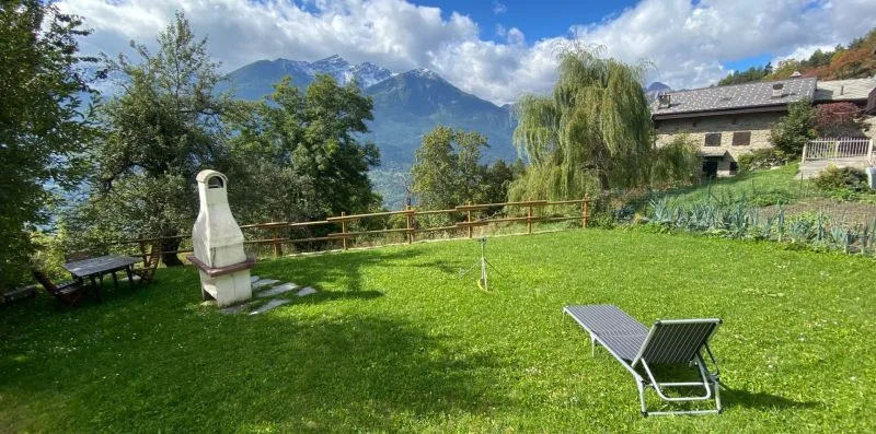 A grassy outdoor yard with seating, trees, and mountains in the background.