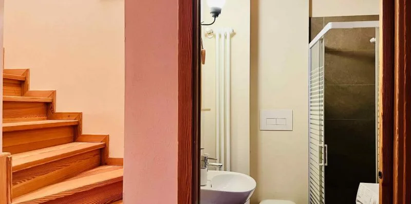 A bathroom with a sink and glass shower beside a wooden staircase.