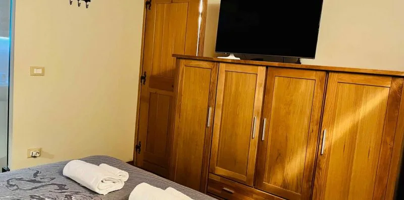 A bedroom with a wooden cabinet, television, and neatly folded towels on the bed.