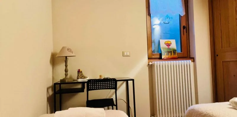 A bedroom with a desk and chair beside a window and radiator.