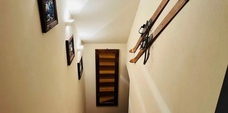A narrow hallway displays framed pictures and skis mounted along the wall.