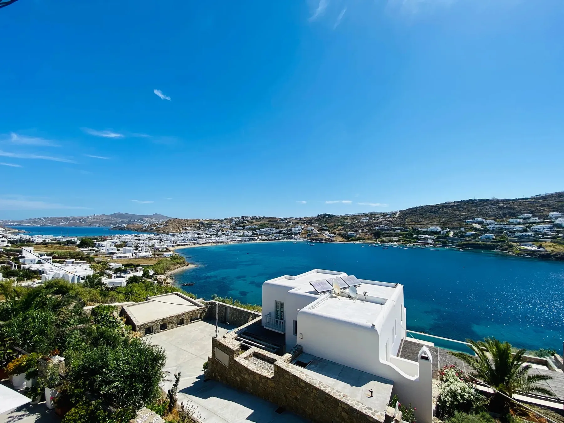 A white building overlooks a blue bay and the surrounding hillside.
