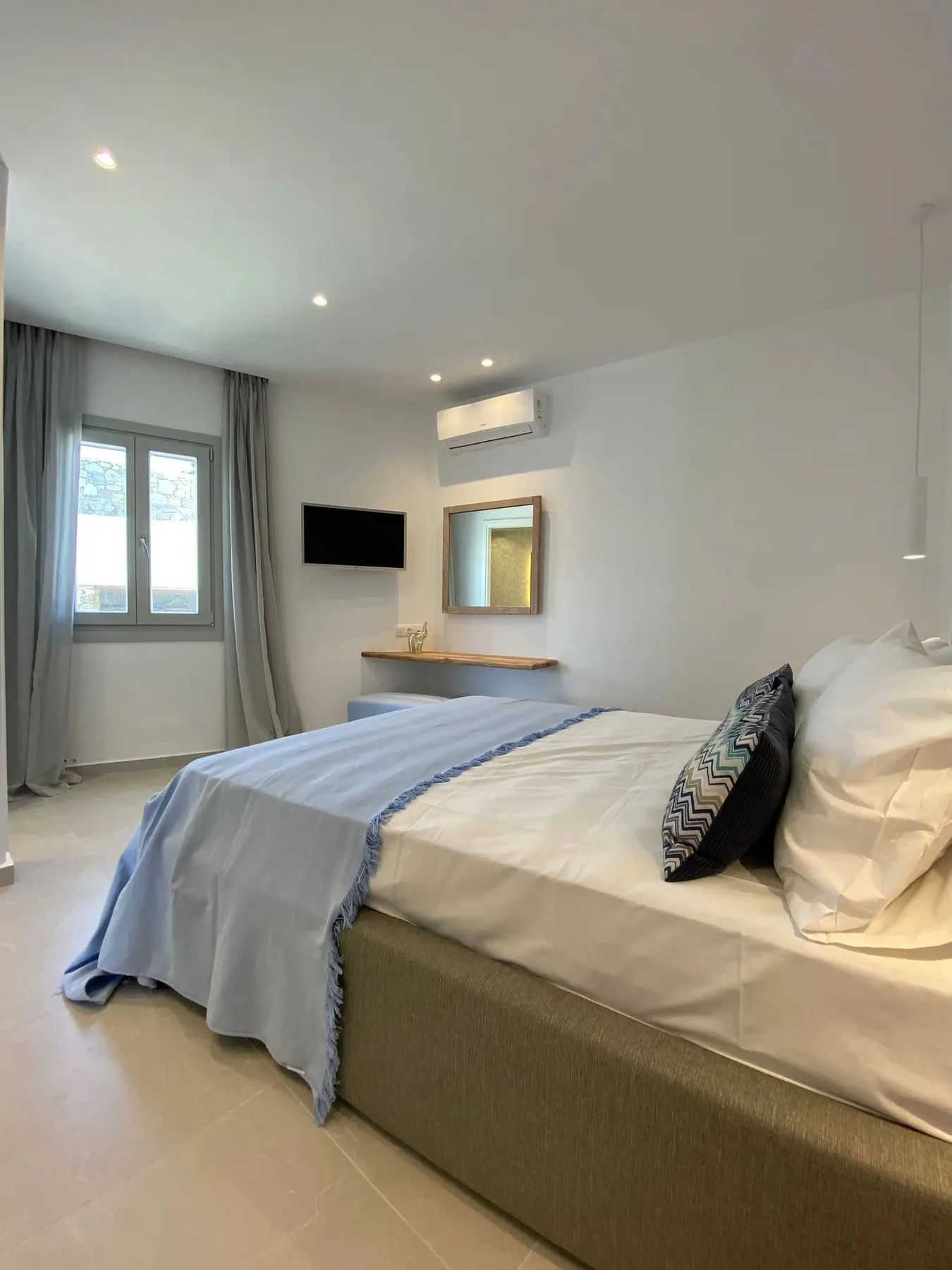 A bedroom with a neatly made bed and a window beside it.