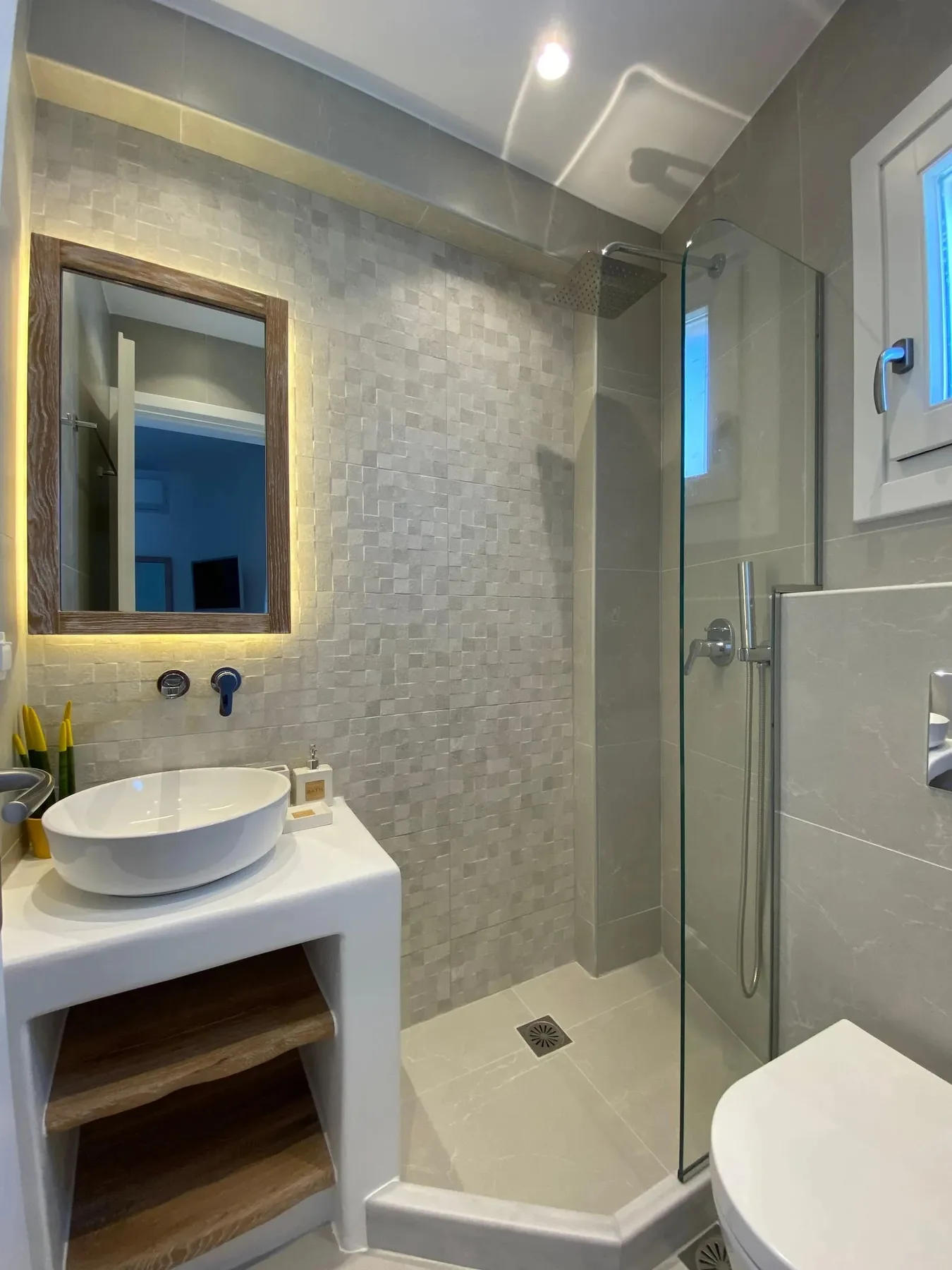 A tiled bathroom has a sink, mirror, and glass shower.