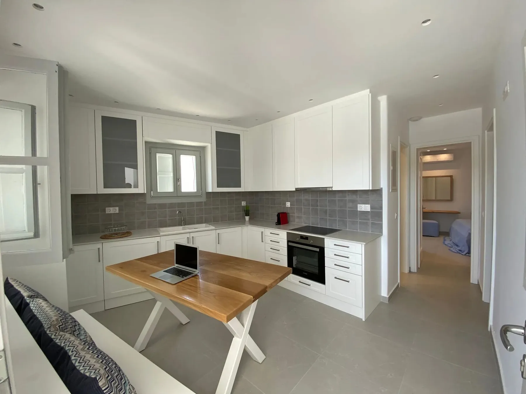 A bright kitchen with white cabinets, gray counters, and a wooden table.
