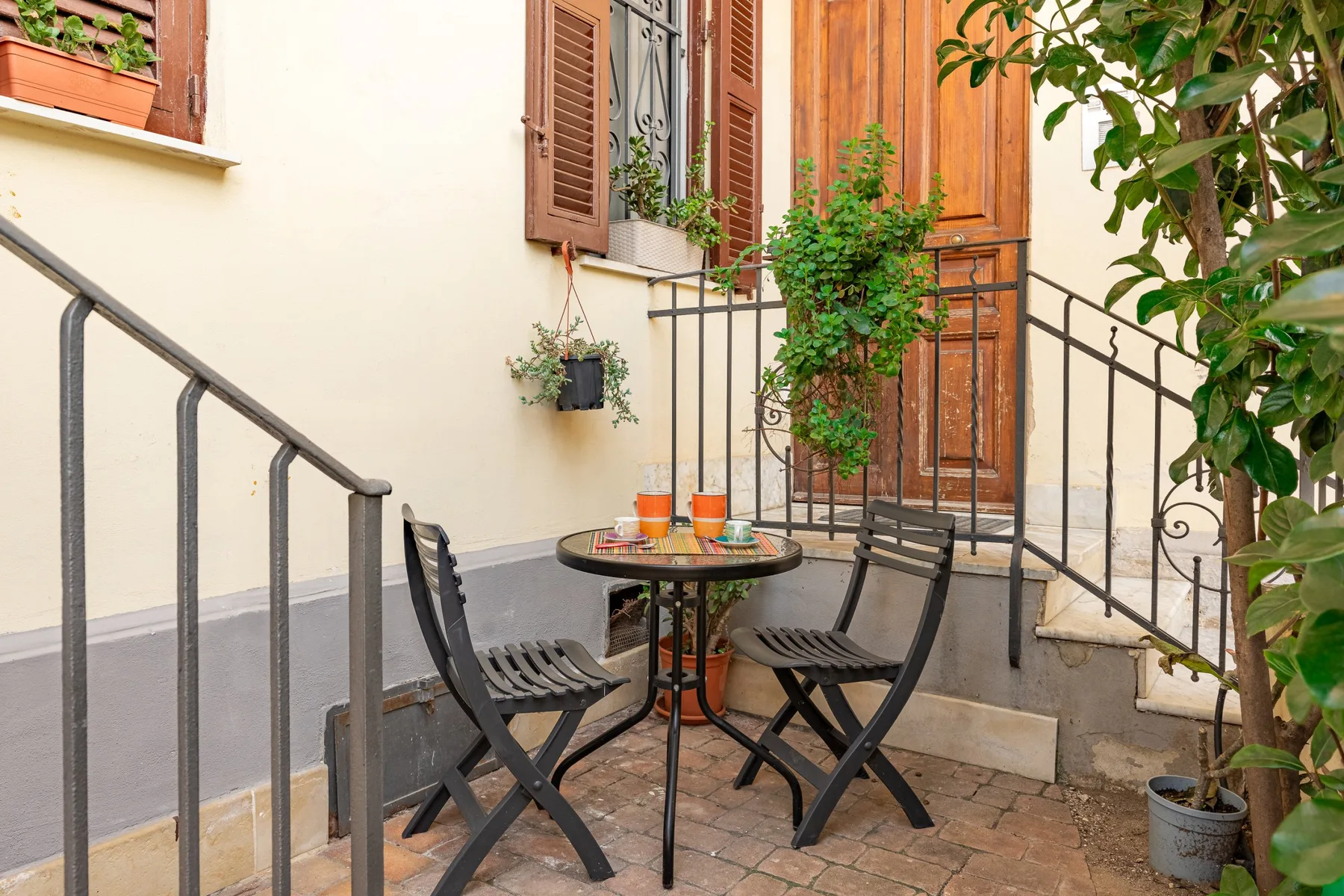 A small outdoor patio has a round table, seating, and potted plants.