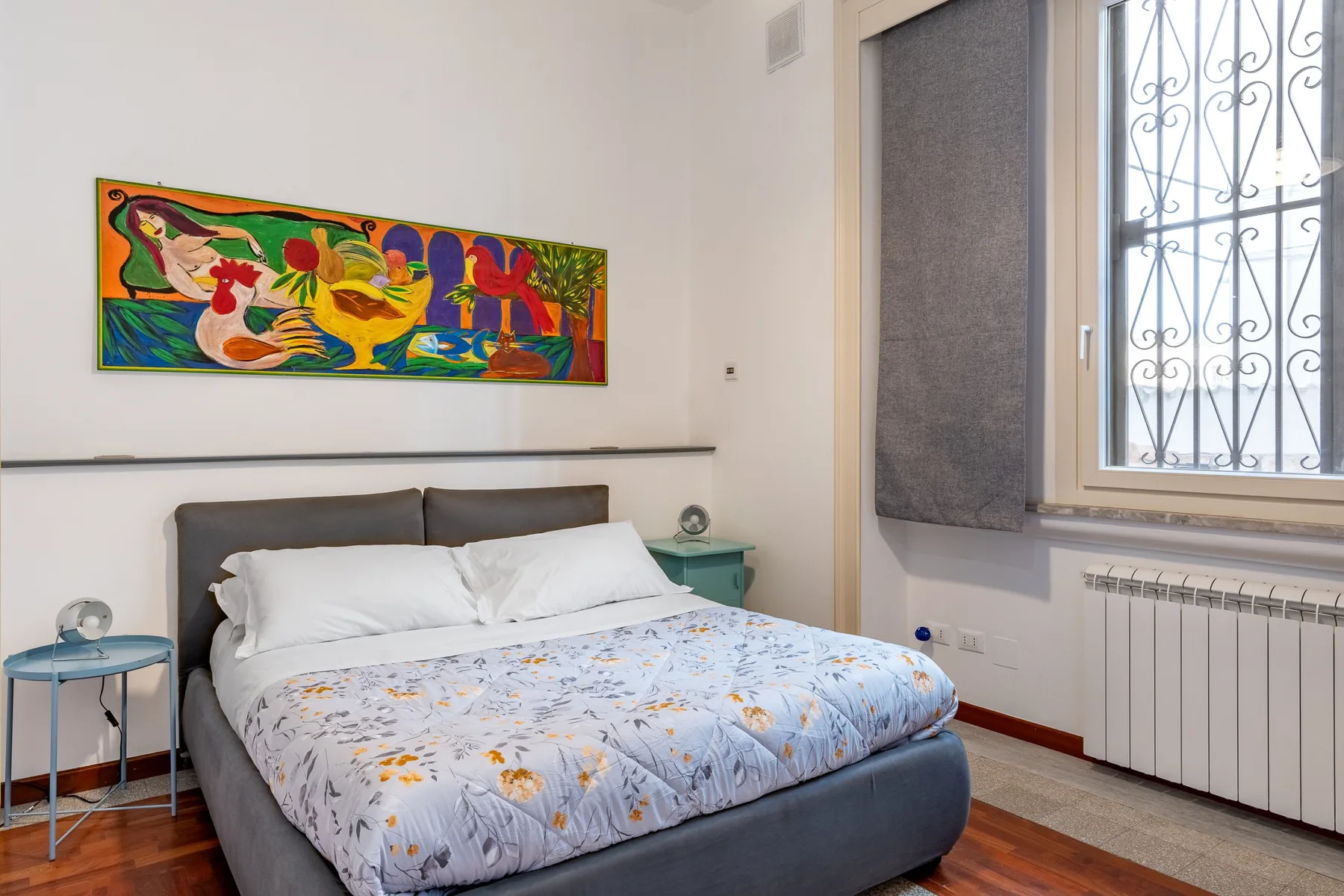 A bedroom with a bed beneath a colorful painting.