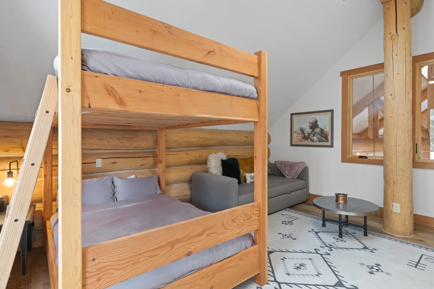 A wooden bunk bed sits beside a small seating area in a bright room.