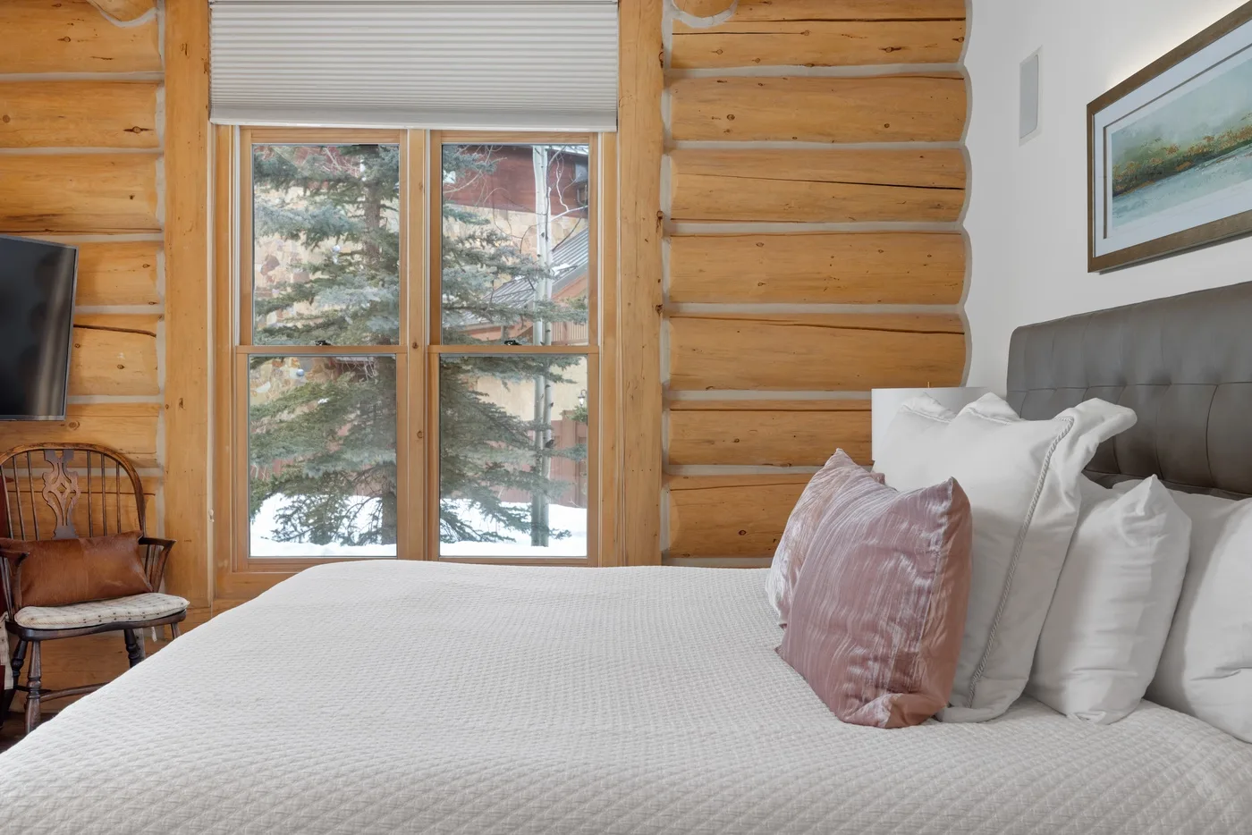 A bedroom with a bed beside a large window and wood-paneled walls.