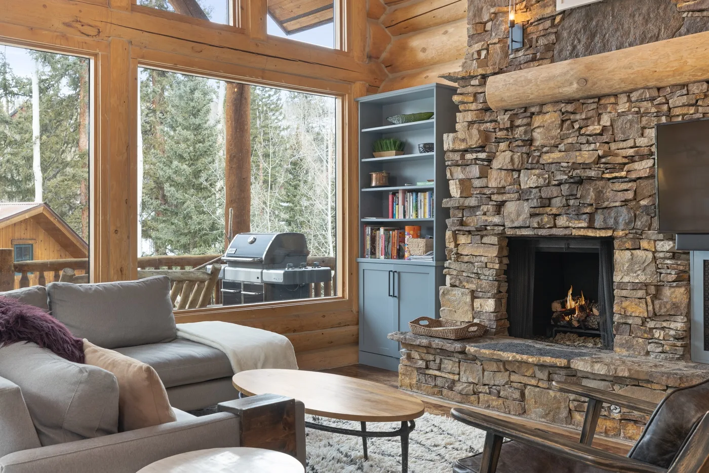 Una sala rústica con asientos, una chimenea de piedra y grandes ventanas.