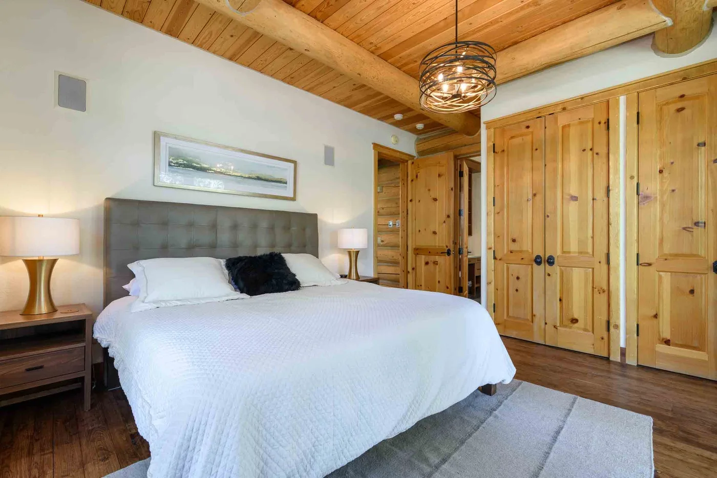 A bedroom with a large bed, wooden doors, and a wood-paneled ceiling.