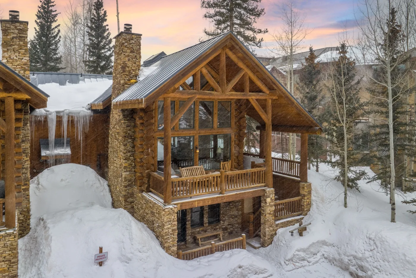 A timber lodge with a covered porch stands among snow-covered trees.