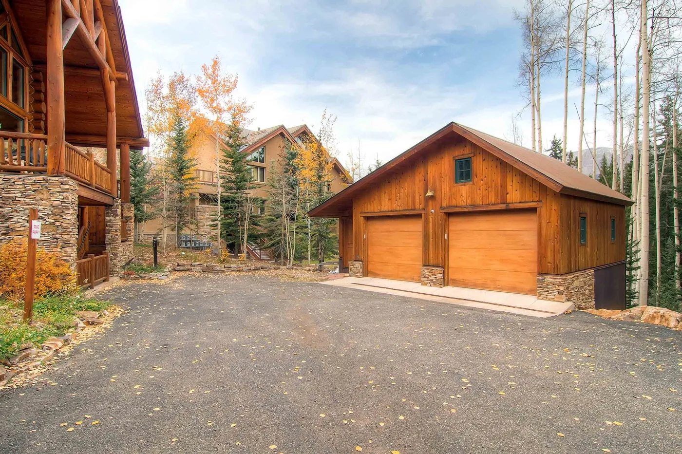 A wooden garage with two doors stands beside a paved driveway and timber buildings.