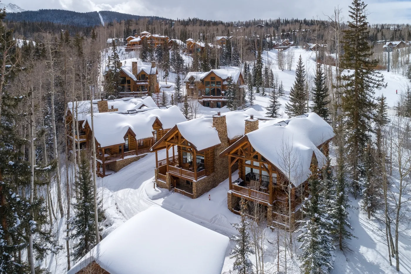 Snow-covered cabins sit among pine trees on a wooded hillside.