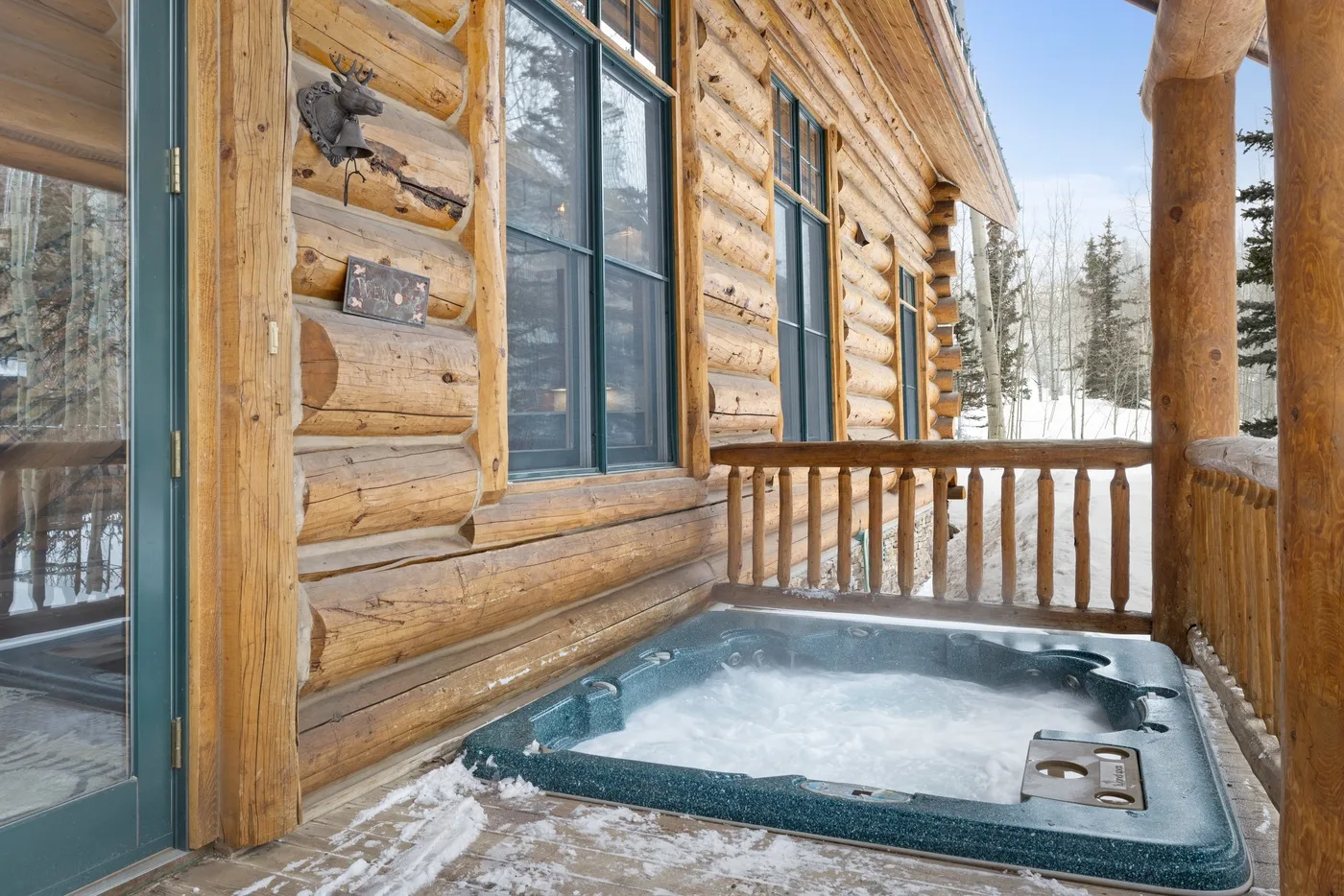 A wooden cabin deck with an outdoor hot tub beside the log wall.