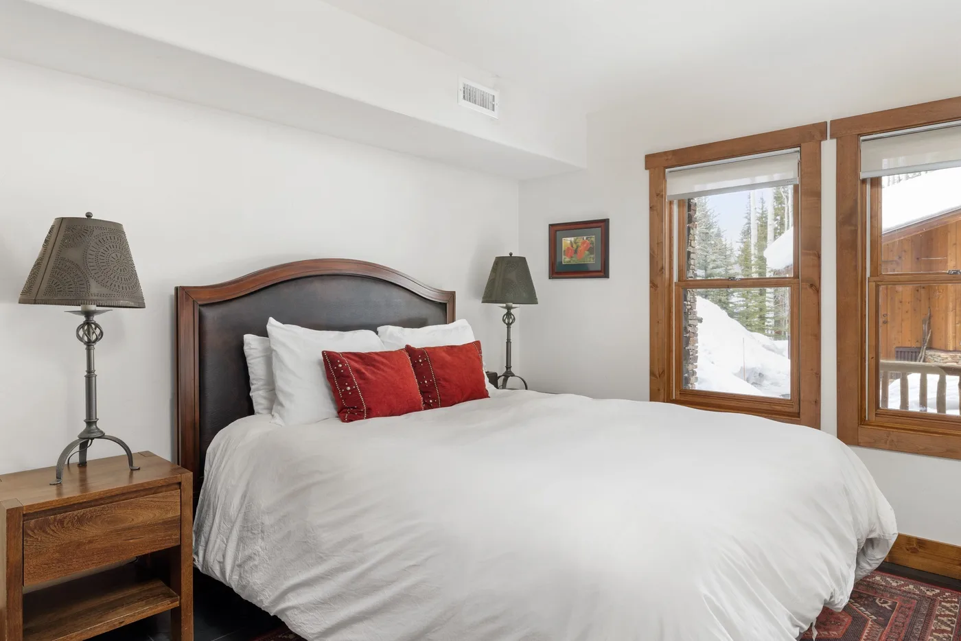 A bedroom with a large bed, bedside tables, and windows overlooking a snowy landscape.