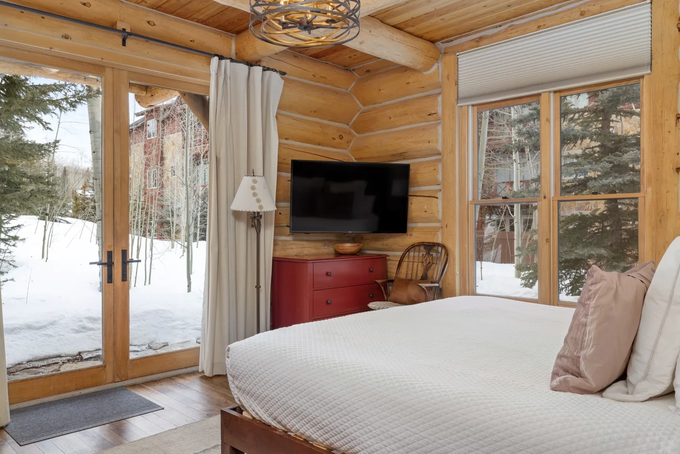 A bedroom with a large bed, television, and windows overlooking a snowy landscape.