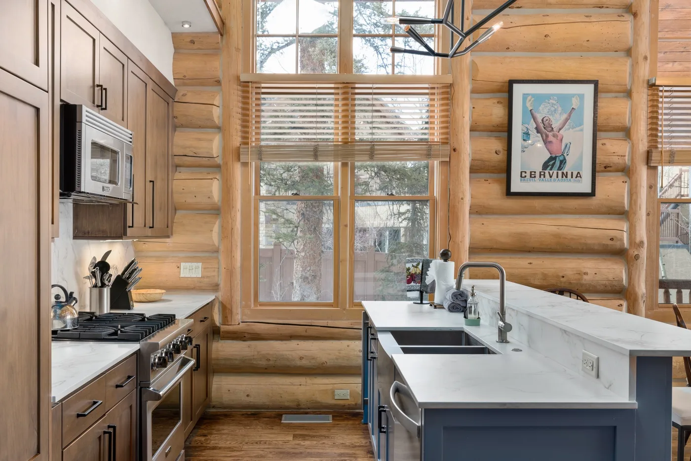 A log-cabin kitchen with a central island and large windows.