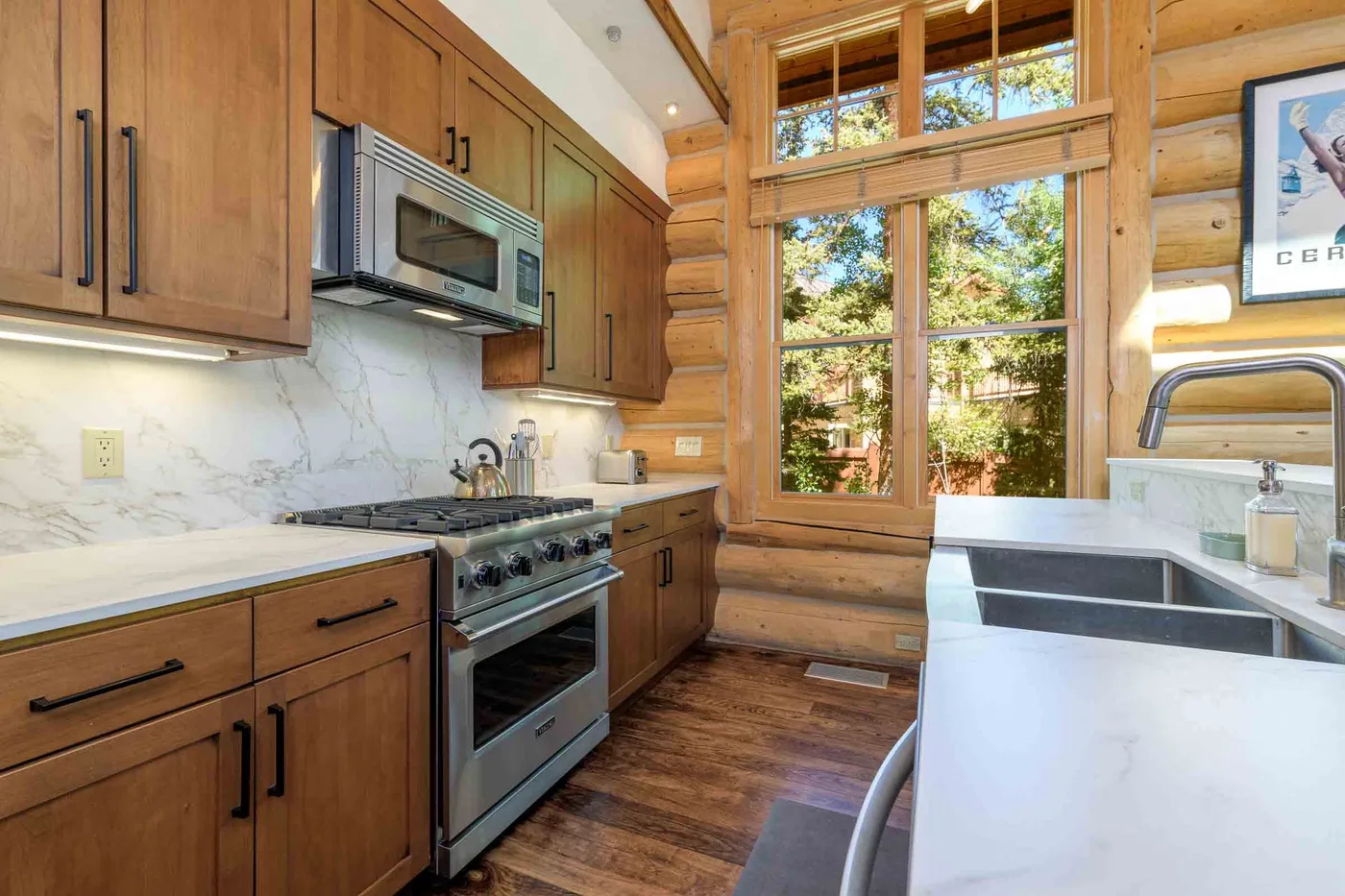 A wood-paneled kitchen with a range and a large window overlooking trees.