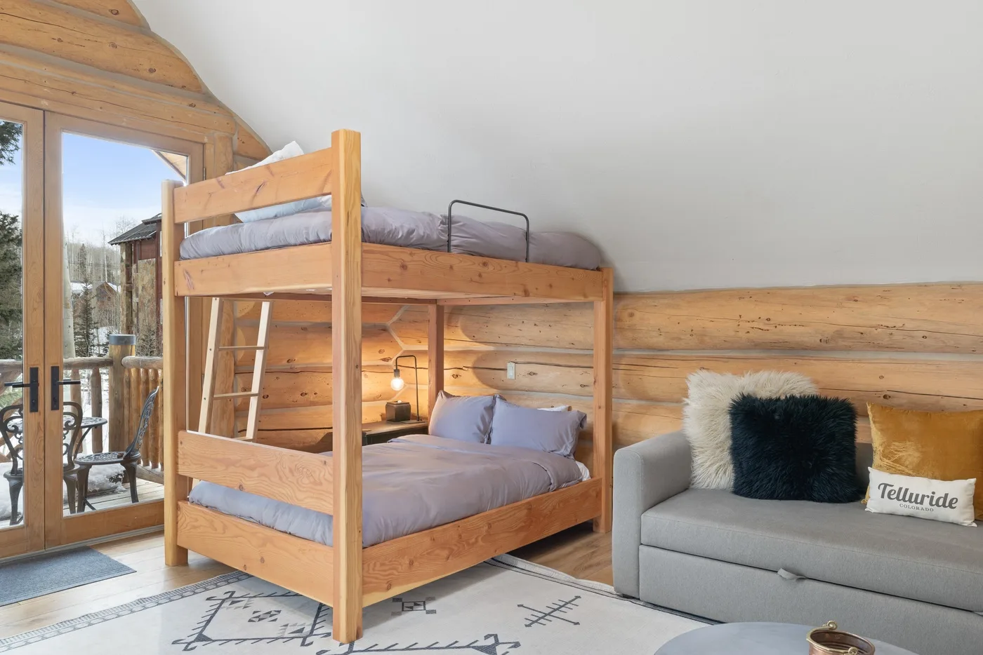 A bedroom with a wooden bunk bed beside a gray sofa and glass doors.