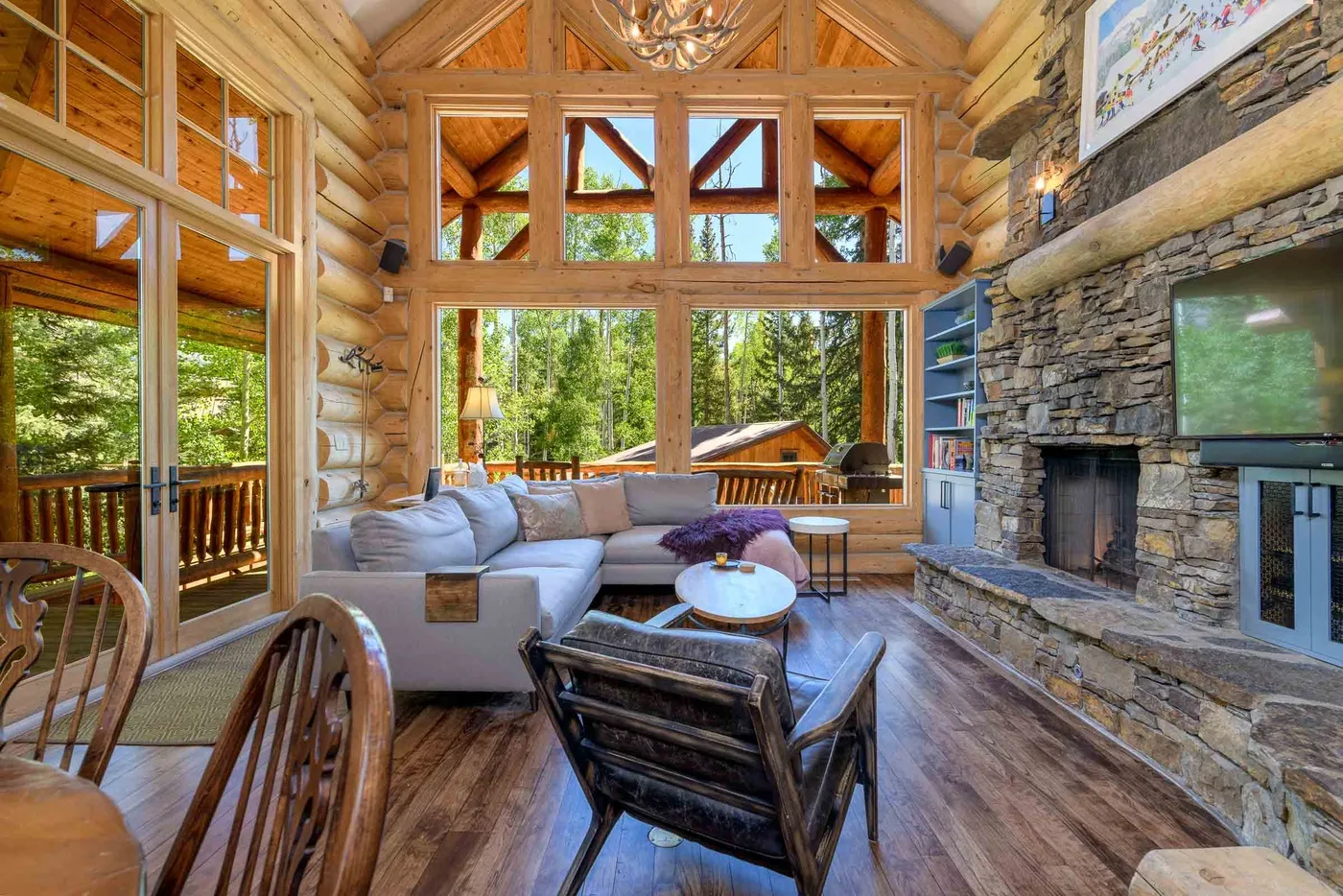 A timber living room with large windows, seating, and a stone fireplace.