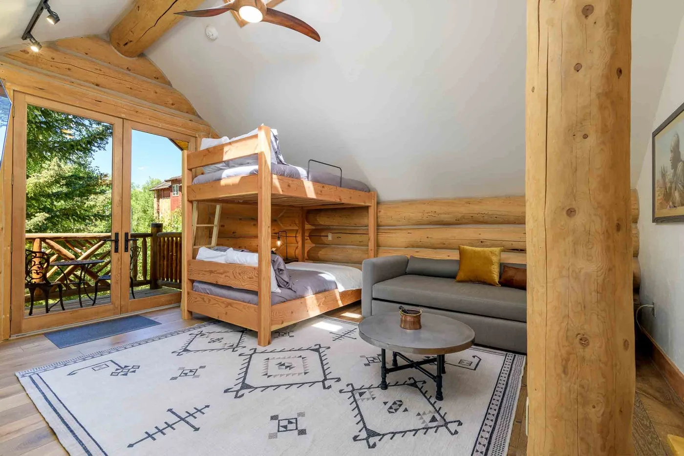 A timber-lined bedroom with bunk beds and a seating area beside glass doors.