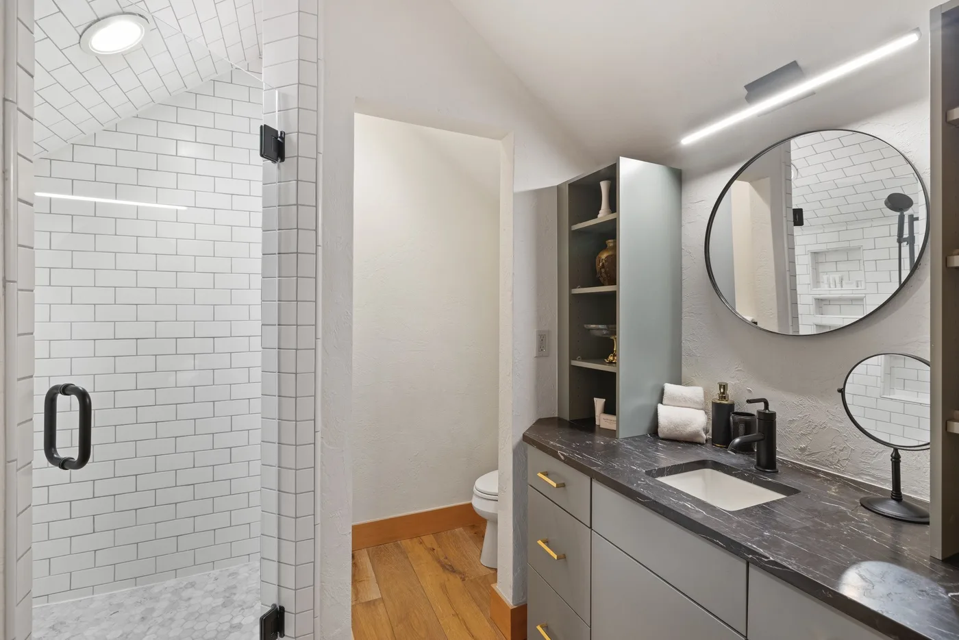A bright bathroom with a tiled shower and a long vanity with mirrors.