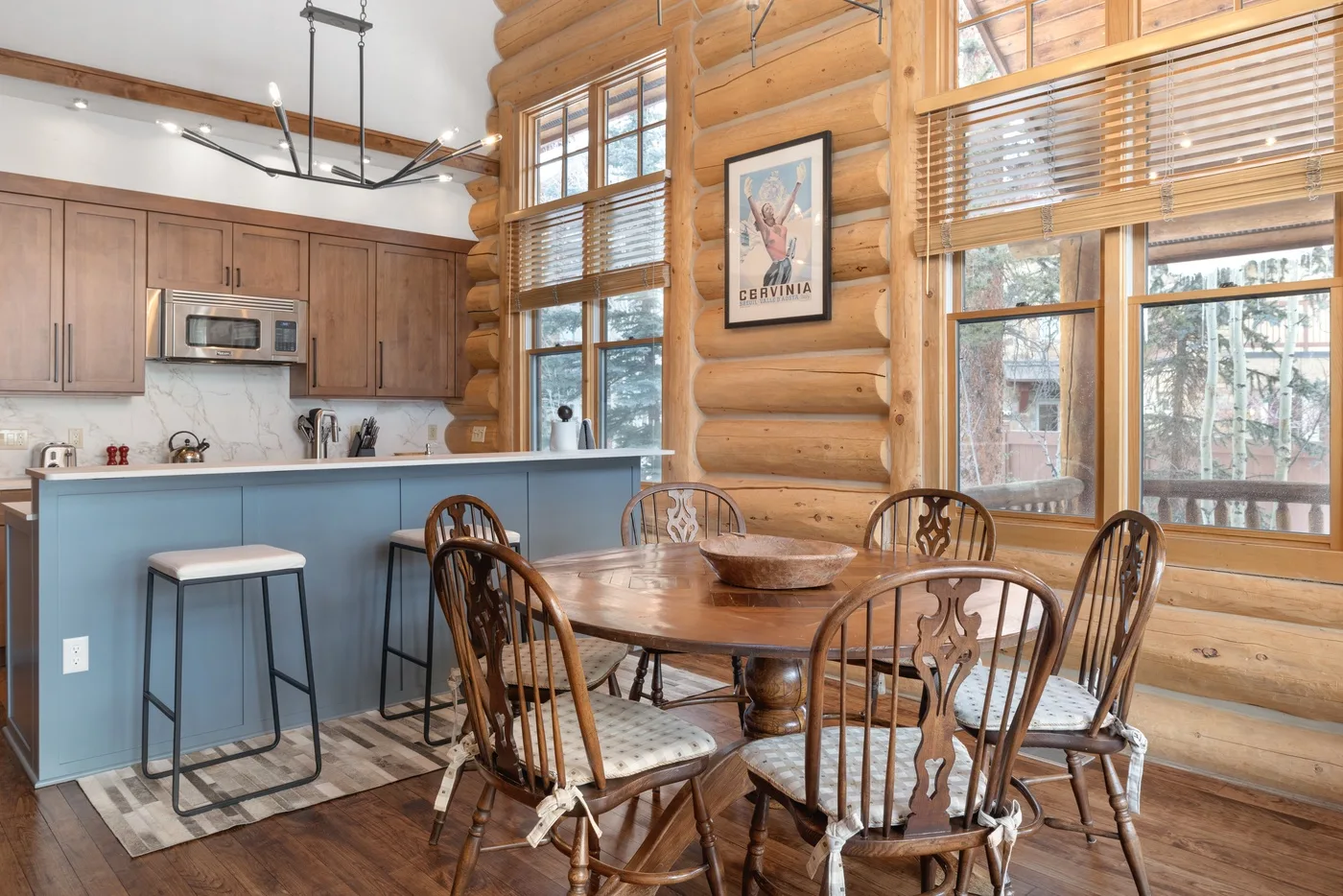 A dining area with a wooden table beside a kitchen and large windows.