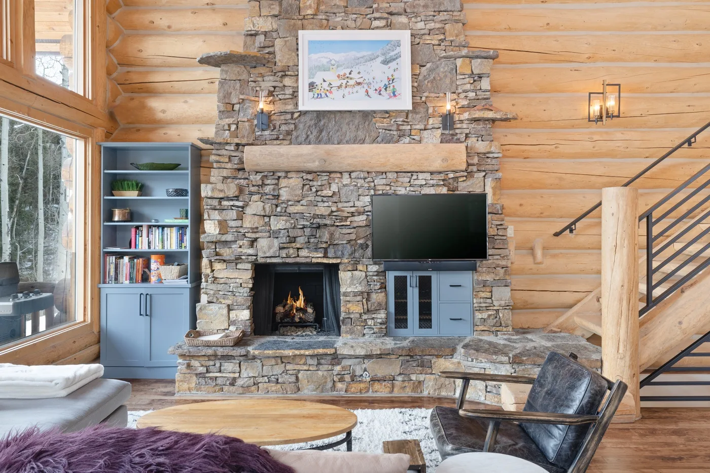 A log-walled living room features a stone fireplace and seating.