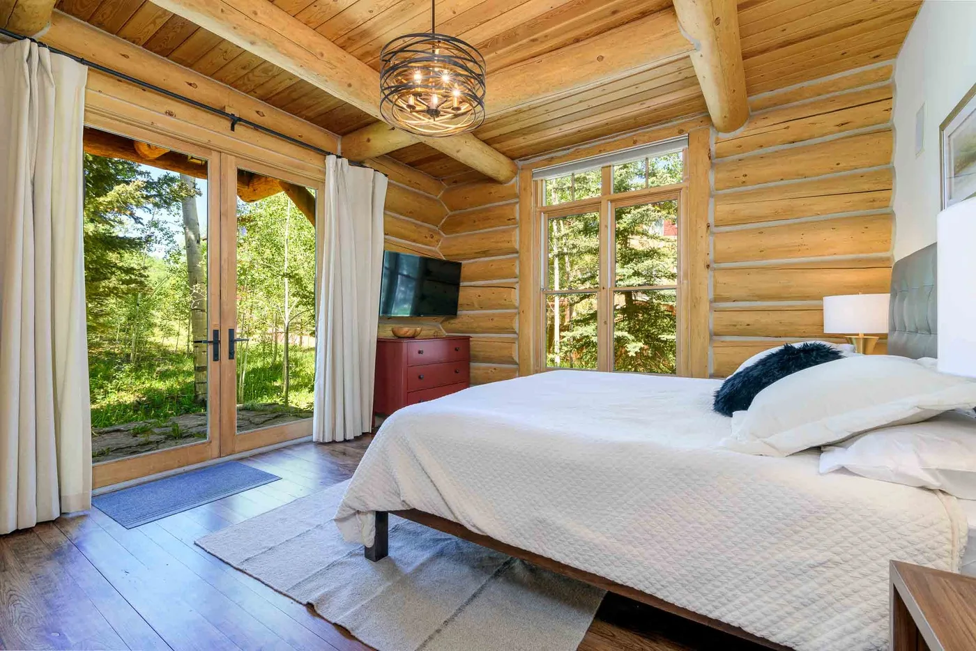 A bedroom with a bed beside large windows overlooking trees.