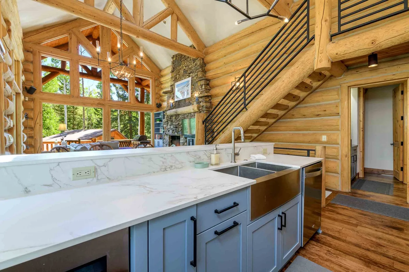 A kitchen island faces a stone fireplace and staircase in a timber interior.