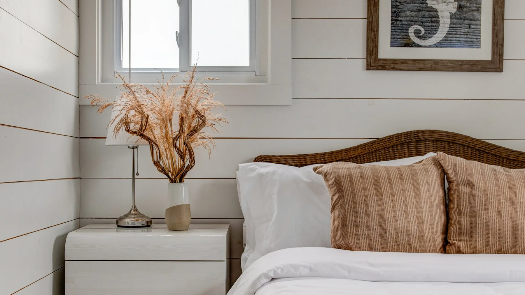 Un dormitorio con ropa de cama blanca, cojines a rayas y una mesita de noche.