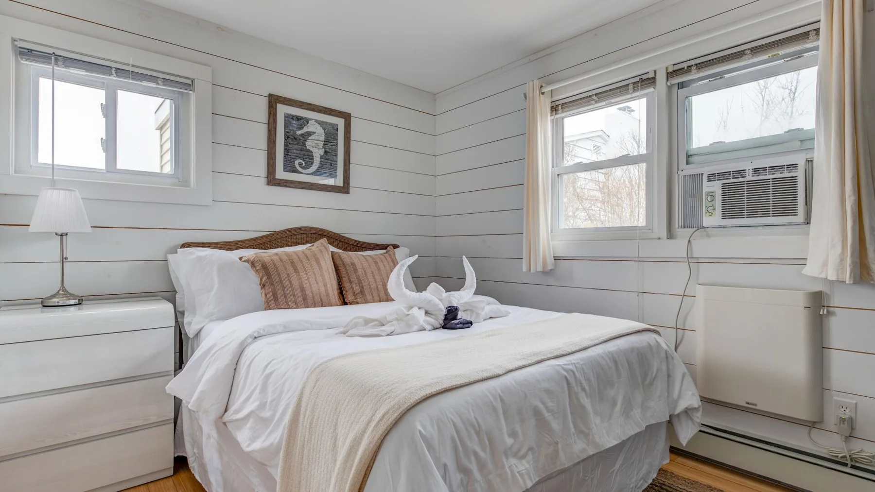 Dormitorio con una cama tendida, ropa de cama clara y ventanas.