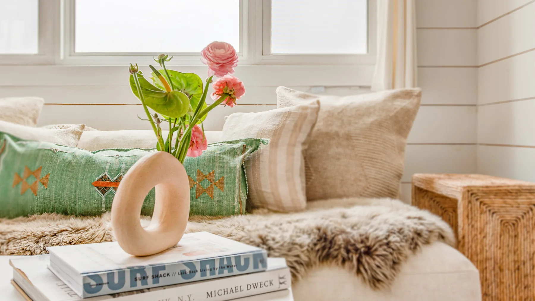 Una luminosa zona de estar con cojines estampados y flores sobre una mesa.