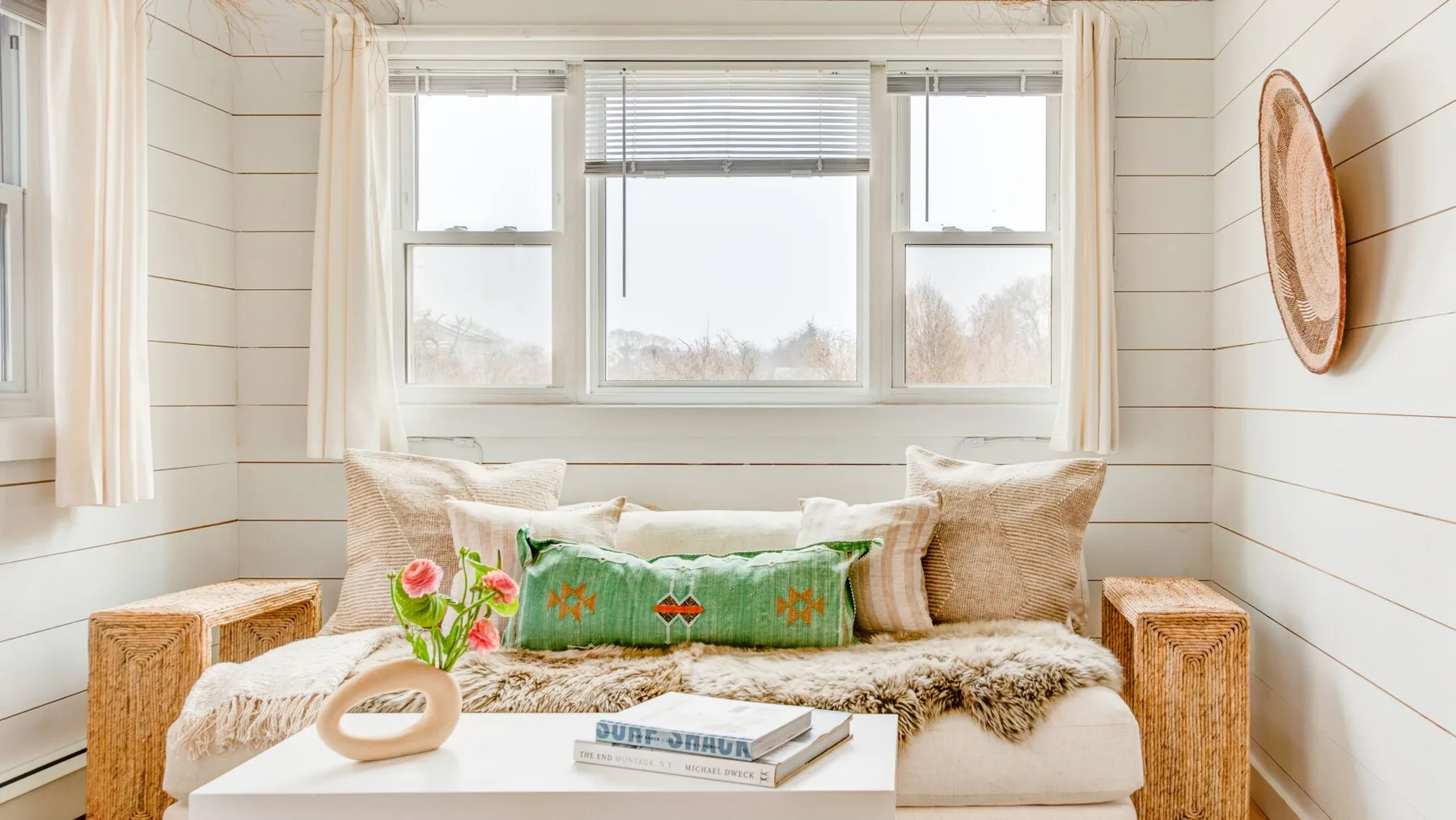 Una luminosa zona de estar tiene un sofá bajo una ventana amplia y una mesa baja delante.