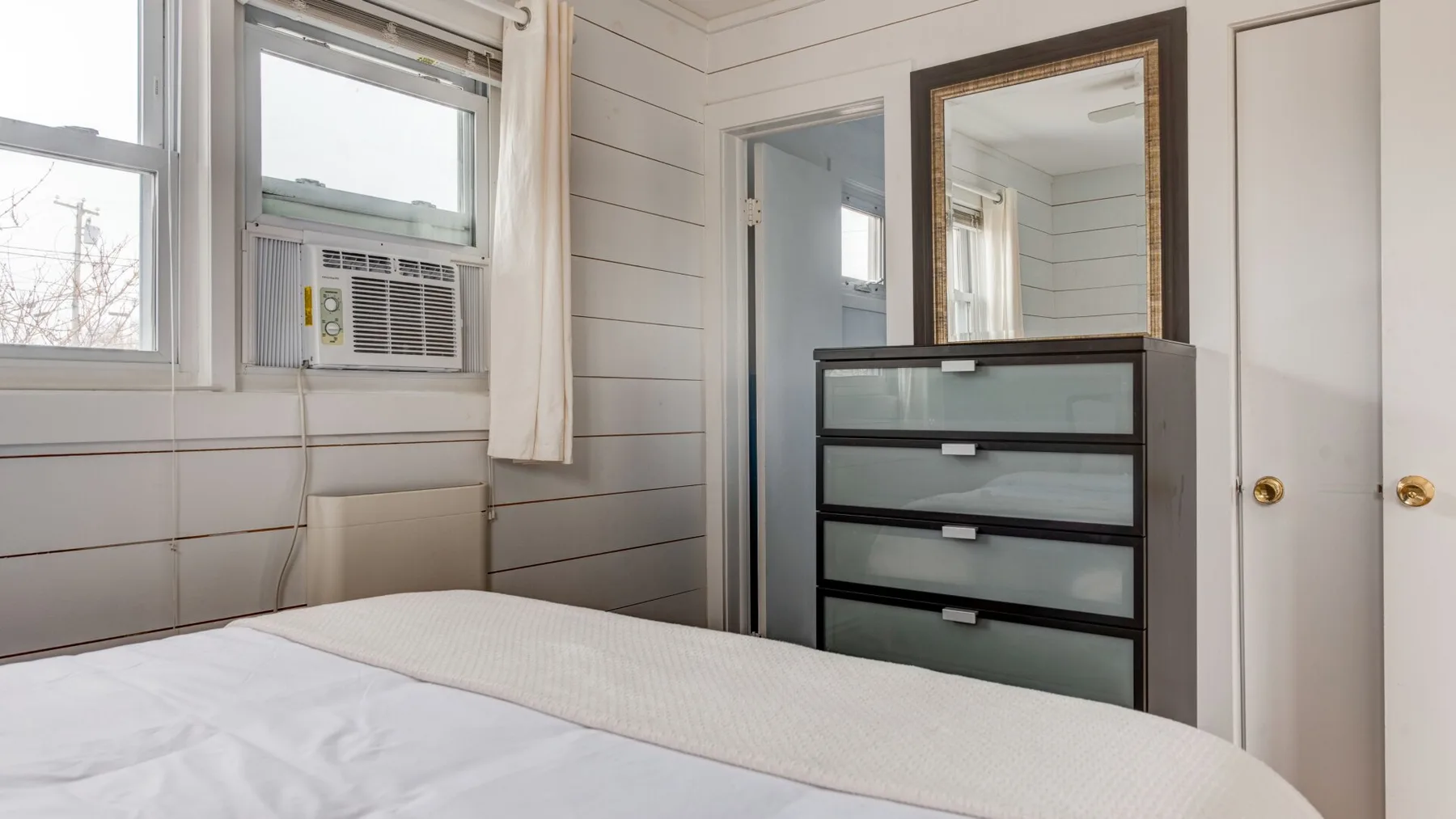 Un dormitorio con una cama, una cómoda oscura y un espejo de pared.