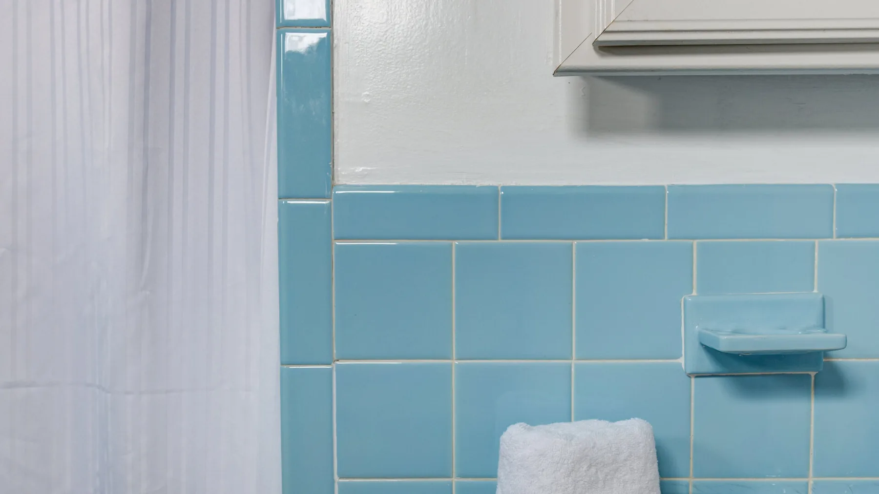 Una pared de baño con azulejos, una cortina de ducha y un pequeño estante.