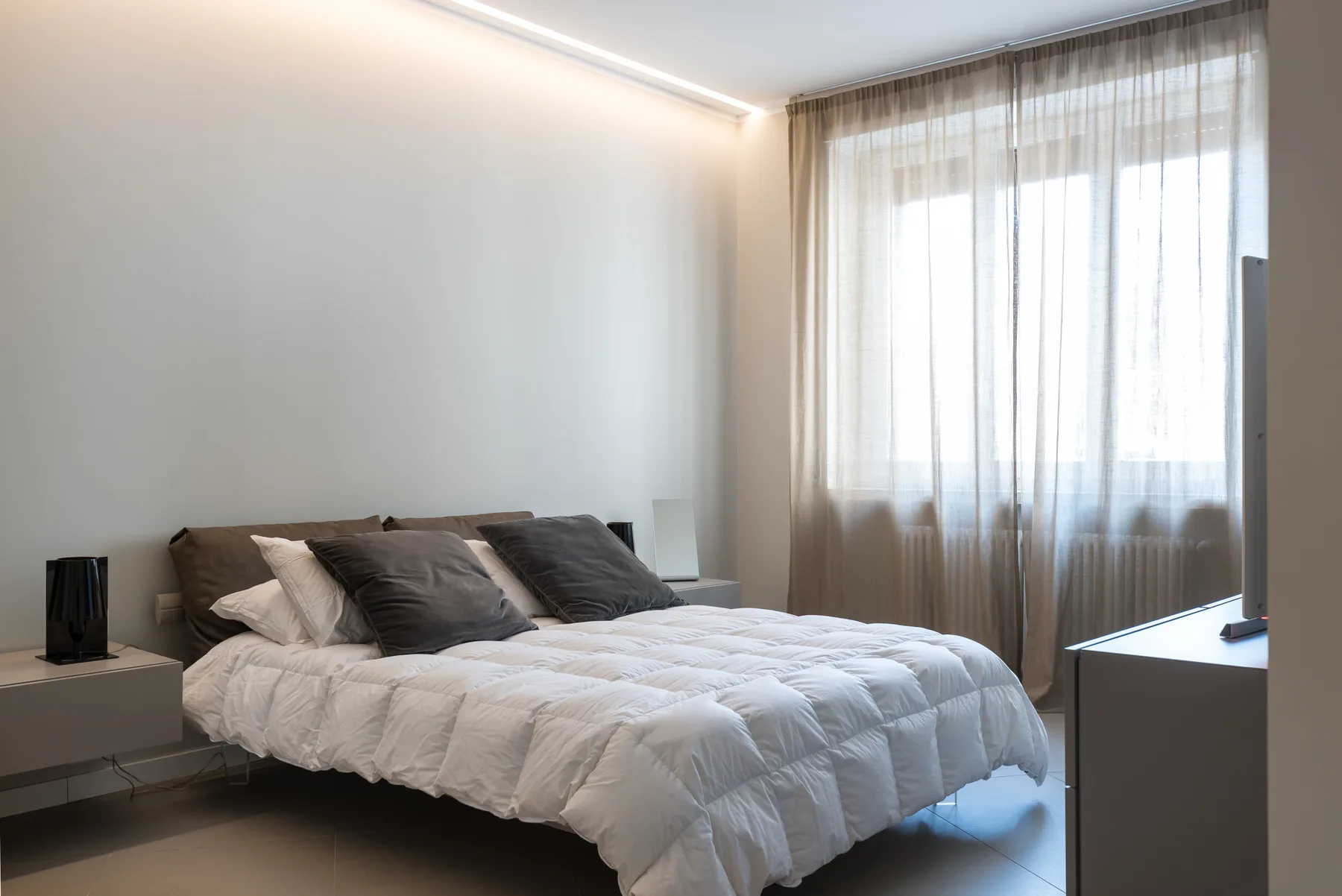 A bedroom with a bed beneath a large curtained window.