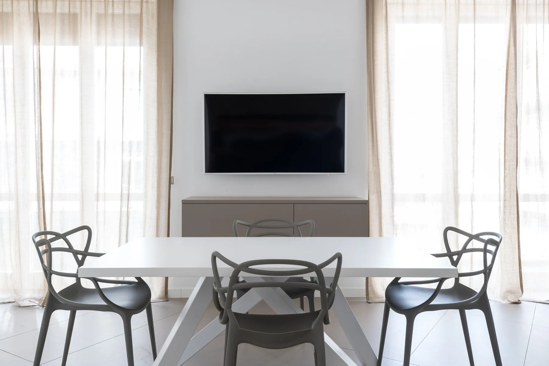 A bright dining area with a white table, seating, and a television on the wall.