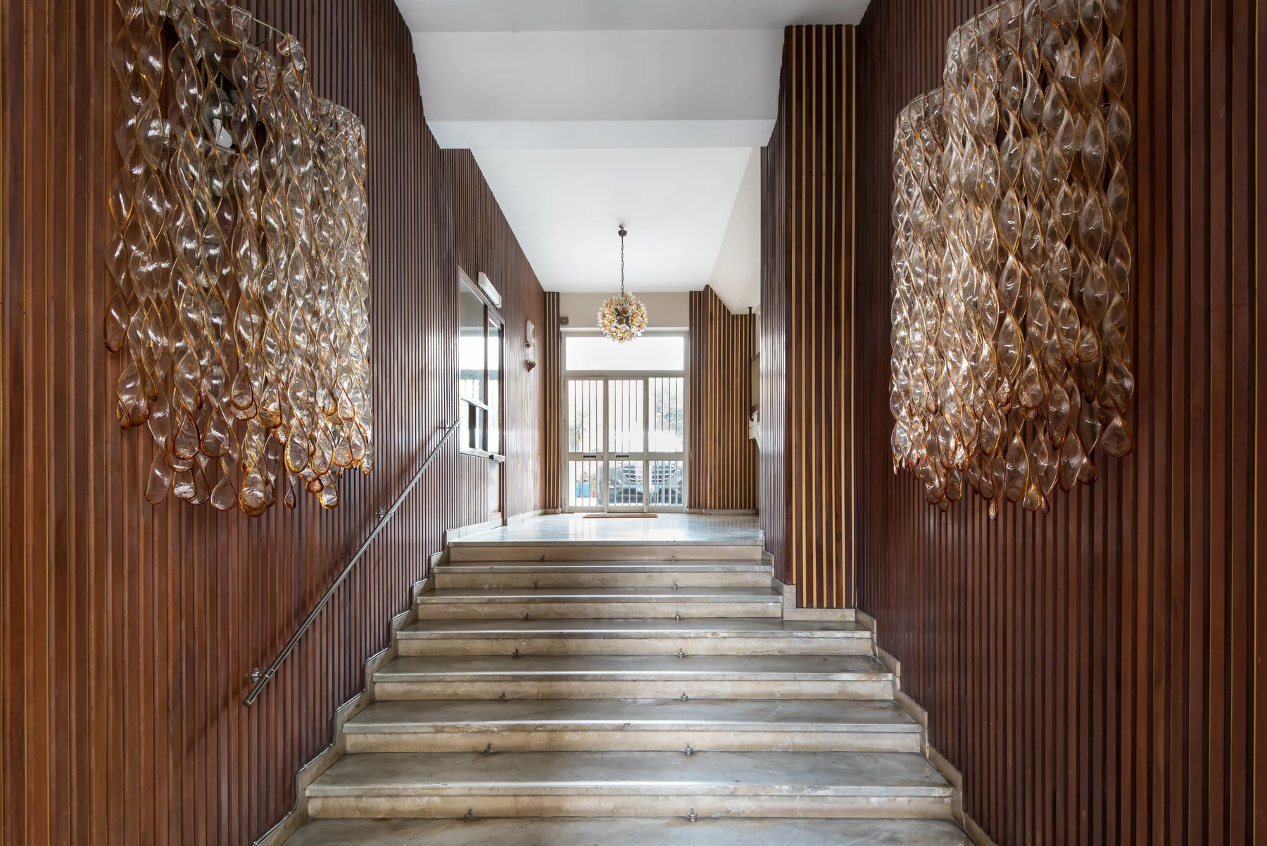 A wide staircase rises between wood-paneled walls toward a bright landing.