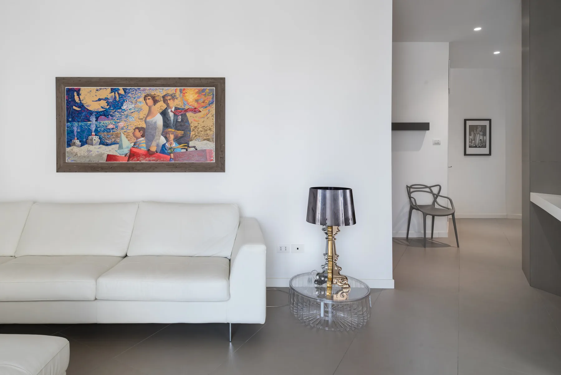 A living room with white seating, a framed painting, and a glass side table.