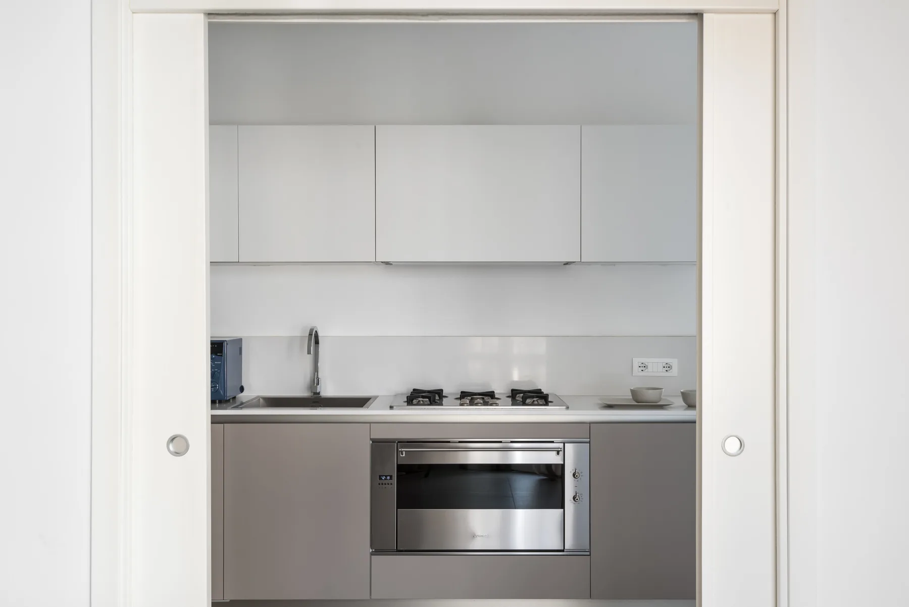 A modern kitchen with white cabinets, a cooktop, and a built-in oven.