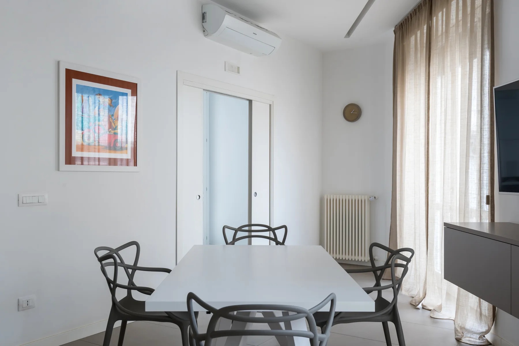 A dining area with a table and chairs beside a tall curtained window.